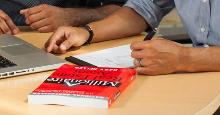 Empresarios revisando el plan de negocios de una agencia inmobiliaria con el libro The Millionaire Real Estate Agent